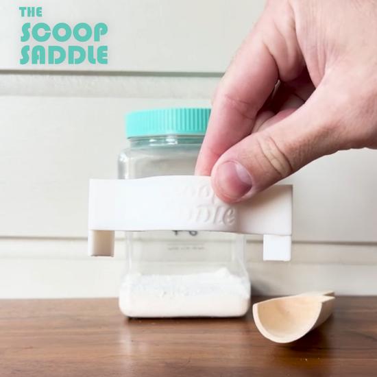 Video demonstration showing how to clip The Scoop Saddle laundry scoop holder onto a Buff City Soap detergent jar and insert a wooden scoop for easy organization.