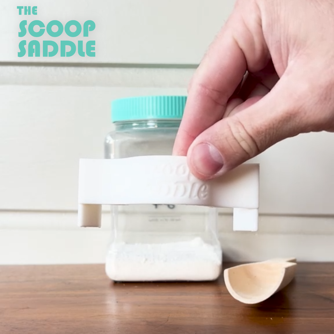 Video demonstration showing how to clip The Scoop Saddle laundry scoop holder onto a Buff City Soap detergent jar and insert a wooden scoop for easy organization.